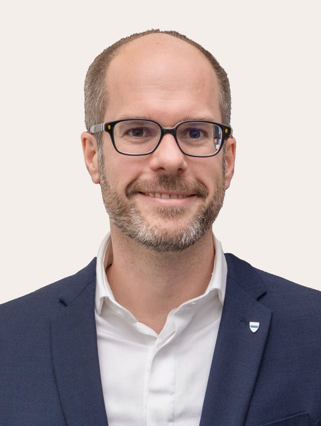 Ein Foto von Ernst Guggisberg vor beigem Hintergrund.